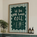 Bathroom with a framed quote 'let the good times roll' above a bathtub, featuring green tiles and towels.